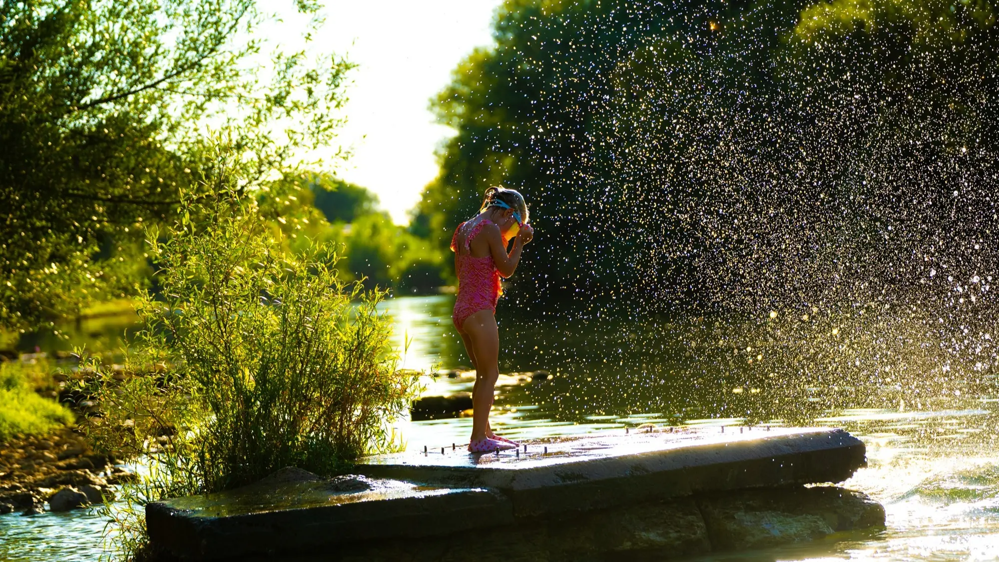 Een kind speelt tussen opspattend water in warm avondlicht